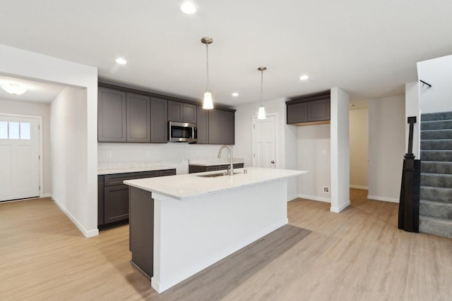 kitchen with light stone countertops, sink, hanging light fixtures, light hardwood / wood-style floors, and a kitchen island with sink