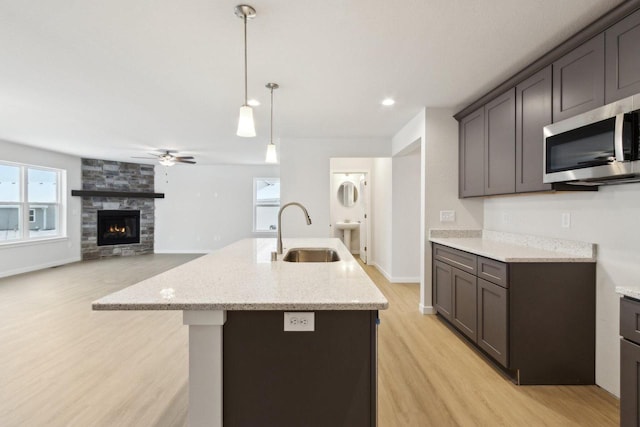 kitchen with a fireplace, ceiling fan, sink, and a kitchen island with sink