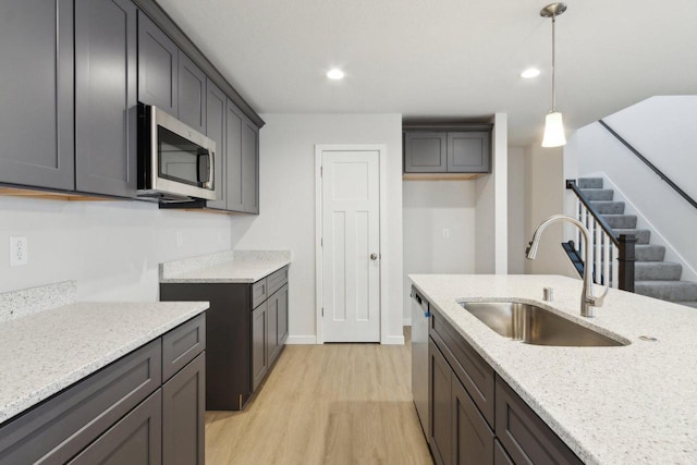 kitchen with light stone counters, stainless steel appliances, sink, decorative light fixtures, and light hardwood / wood-style floors