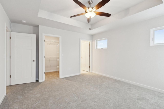 unfurnished bedroom with a raised ceiling, a walk in closet, ceiling fan, light colored carpet, and a closet