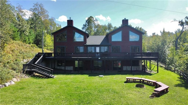 back of property with a wooden deck, a lawn, and a fire pit