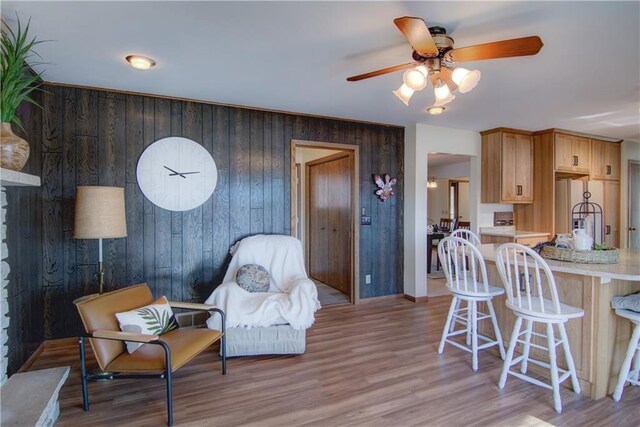 living room with a fireplace, wood walls, ceiling fan, and light hardwood / wood-style floors