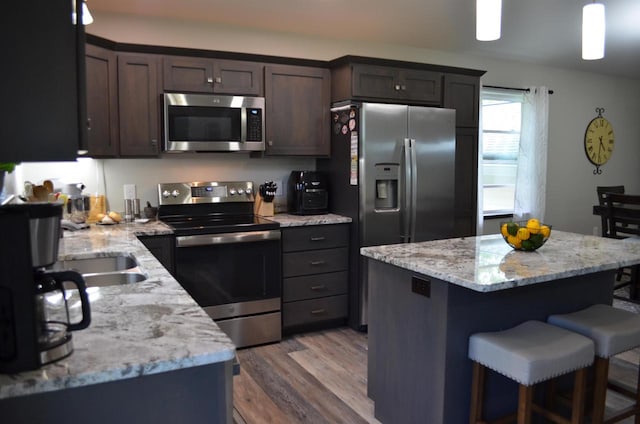 kitchen featuring stainless steel appliances, light stone counters, wood-type flooring, and decorative light fixtures