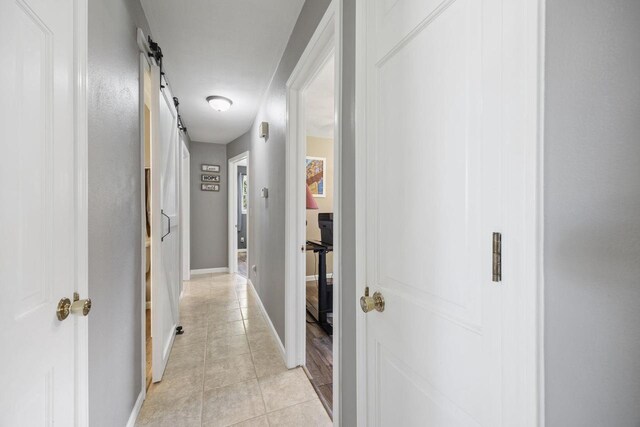 corridor featuring light tile patterned floors, a barn door, and baseboards