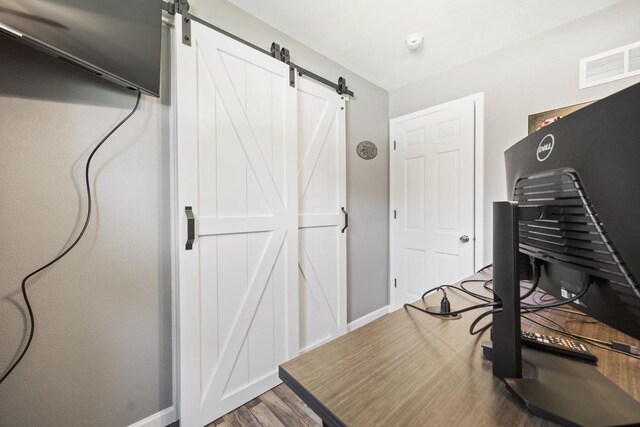 exercise area featuring a barn door, wood finished floors, visible vents, and baseboards