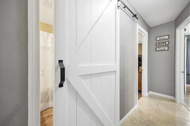 hallway featuring a barn door, baseboards, and light tile patterned flooring