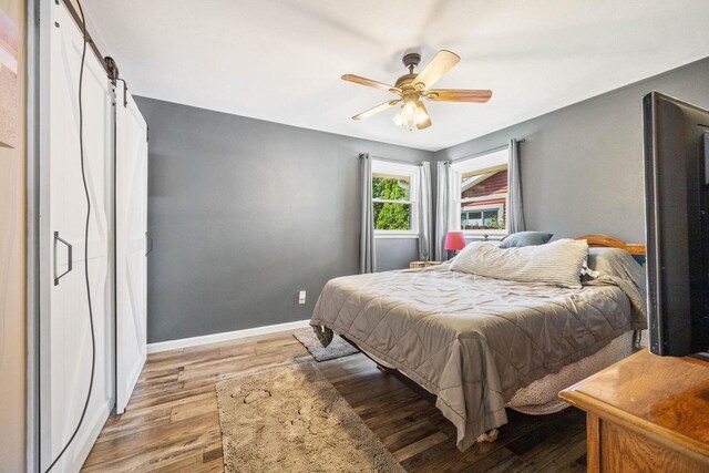 bedroom with light wood-style floors, a barn door, baseboards, and a ceiling fan