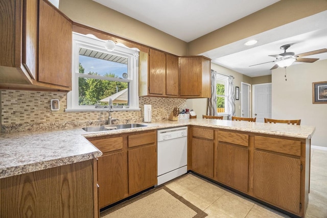 kitchen with light countertops, backsplash, a sink, dishwasher, and a peninsula