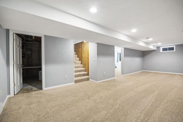 finished below grade area featuring light colored carpet, visible vents, baseboards, and stairs