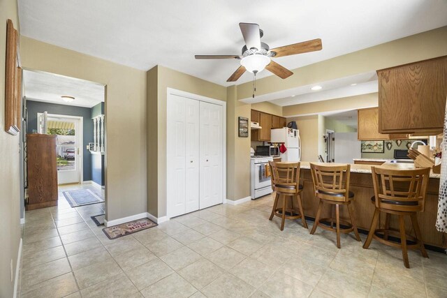 kitchen with white appliances, baseboards, brown cabinetry, a peninsula, and light countertops