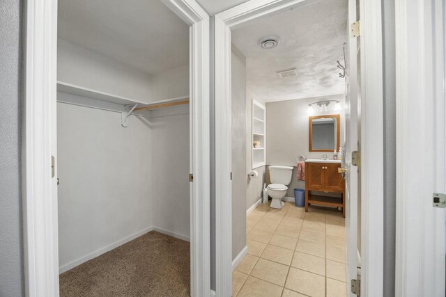 bathroom featuring tile patterned flooring, toilet, visible vents, vanity, and a walk in closet