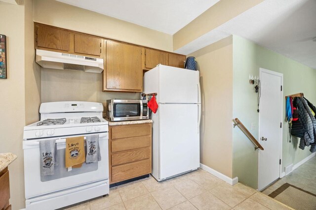 kitchen featuring light tile patterned floors, light countertops, white appliances, under cabinet range hood, and baseboards