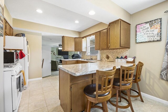 kitchen with gas range gas stove, light countertops, backsplash, brown cabinetry, and a peninsula