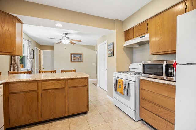 kitchen featuring white appliances, light tile patterned floors, brown cabinetry, a ceiling fan, and under cabinet range hood