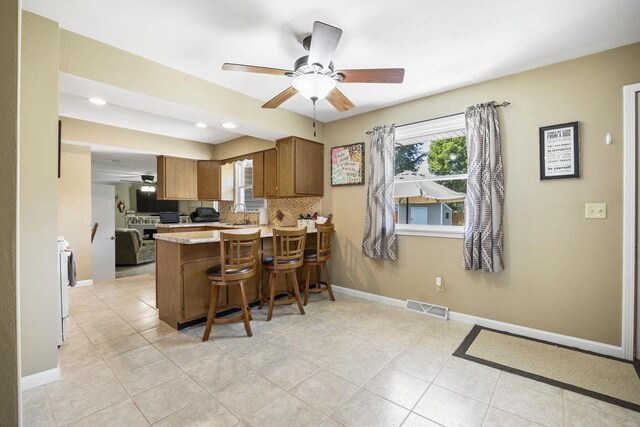 kitchen with brown cabinets, light countertops, visible vents, a peninsula, and baseboards