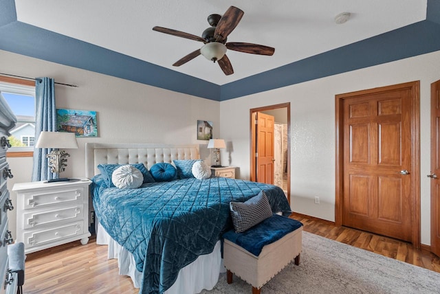 bedroom with light wood-type flooring, ceiling fan, and connected bathroom