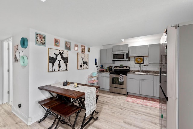 kitchen featuring gray cabinets, light hardwood / wood-style flooring, backsplash, stainless steel appliances, and sink