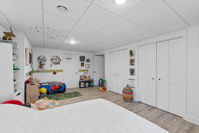 bedroom featuring a drop ceiling, multiple closets, and light hardwood / wood-style flooring