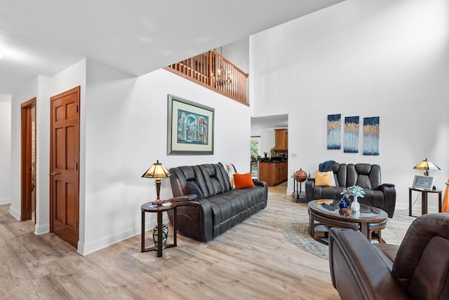 living room with a towering ceiling, an inviting chandelier, and light hardwood / wood-style flooring