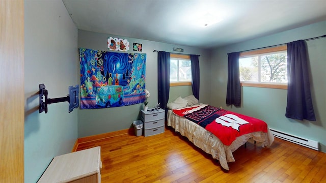 bedroom featuring hardwood / wood-style flooring, multiple windows, and a baseboard heating unit