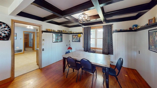 dining room with coffered ceiling, beam ceiling, wood-type flooring, an inviting chandelier, and wood walls