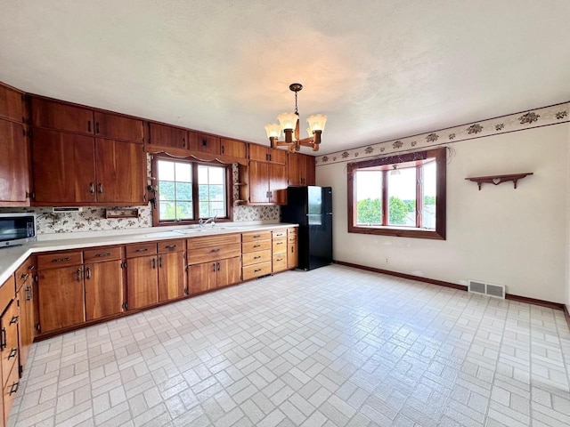 kitchen featuring tasteful backsplash, a healthy amount of sunlight, black refrigerator, and a chandelier