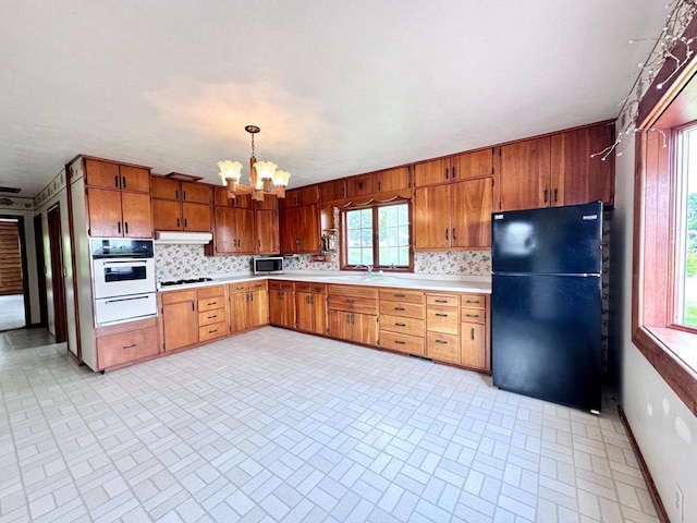 kitchen with black refrigerator, a wealth of natural light, oven, and an inviting chandelier