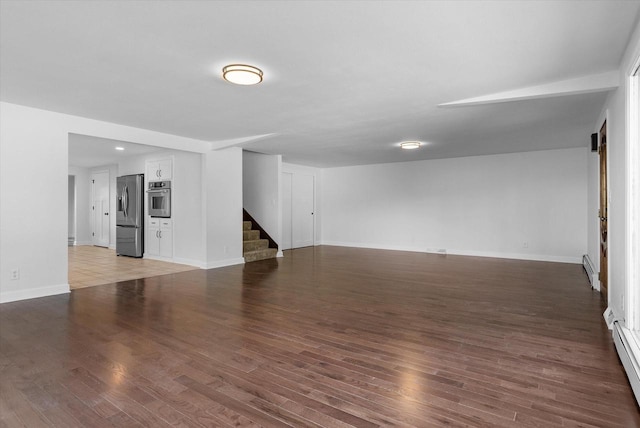 unfurnished living room featuring stairs, baseboard heating, wood finished floors, and baseboards