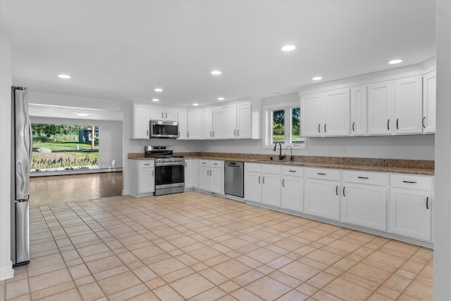 kitchen with recessed lighting, appliances with stainless steel finishes, white cabinets, a sink, and dark stone counters