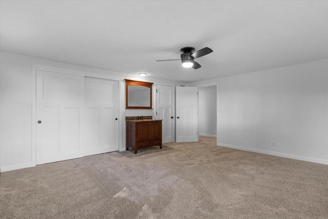 unfurnished bedroom with light carpet, a closet, a ceiling fan, and baseboards