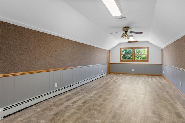 additional living space featuring lofted ceiling, wood finished floors, visible vents, baseboard heating, and wainscoting