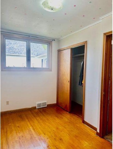 unfurnished bedroom with hardwood / wood-style floors, a closet, and crown molding