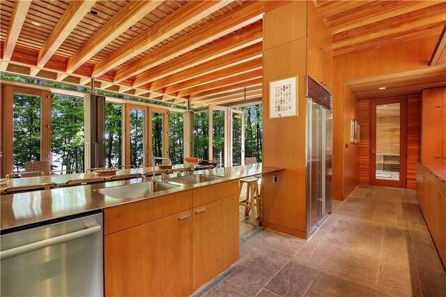 interior space featuring beamed ceiling, a sink, stainless steel countertops, stone tile floors, and appliances with stainless steel finishes