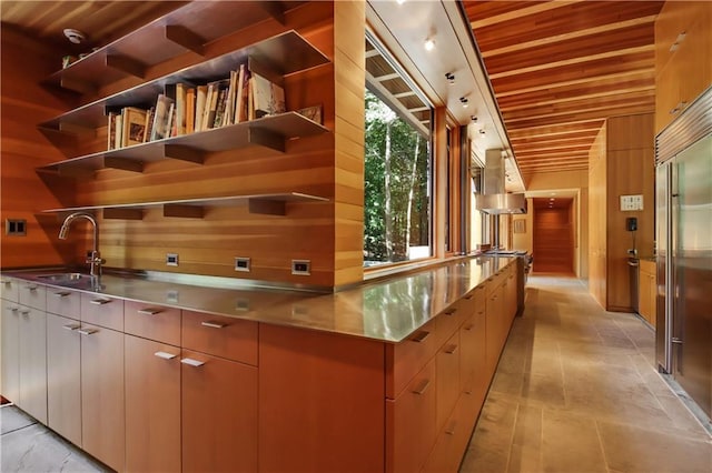 interior space featuring stainless steel built in refrigerator, wood walls, wood ceiling, range hood, and a sink