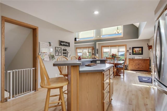 kitchen featuring light wood-type flooring, stainless steel fridge, a chandelier, and a breakfast bar