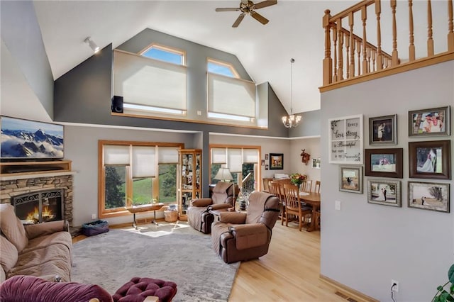 living room with ceiling fan with notable chandelier, high vaulted ceiling, a fireplace, and light hardwood / wood-style flooring