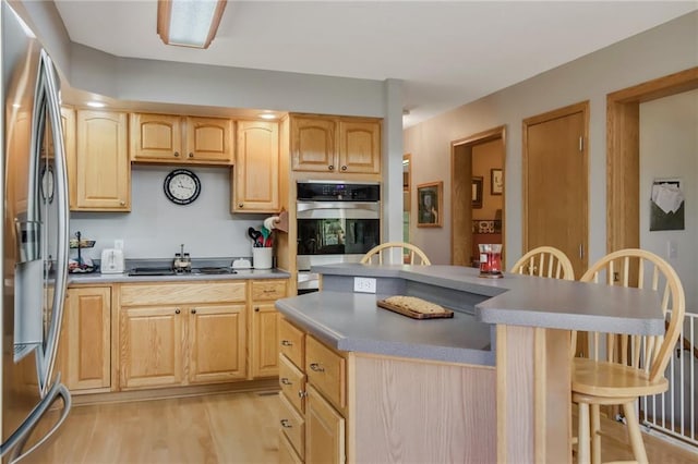 kitchen with light hardwood / wood-style flooring, a kitchen bar, stainless steel appliances, light brown cabinetry, and a center island