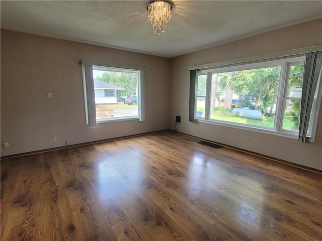 unfurnished room featuring dark wood-type flooring, an inviting chandelier, and a textured ceiling