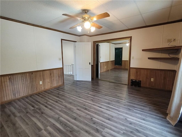 unfurnished living room with dark wood-type flooring, ceiling fan, ornamental molding, and wooden walls