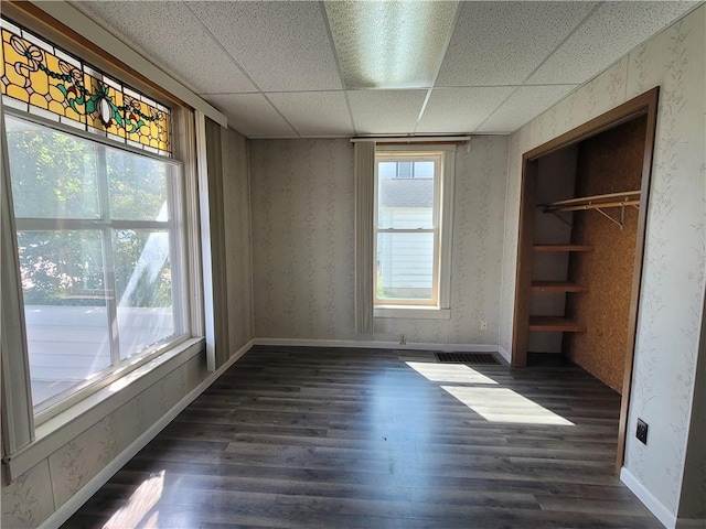 unfurnished bedroom with dark wood-type flooring, a paneled ceiling, and a closet