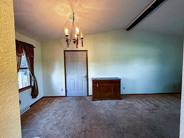 carpeted empty room featuring baseboards, a textured ceiling, an inviting chandelier, and vaulted ceiling with beams