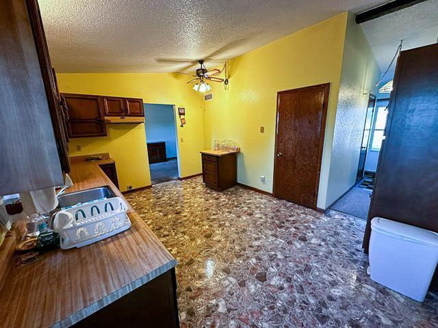 kitchen with lofted ceiling, a sink, ceiling fan, under cabinet range hood, and a textured ceiling