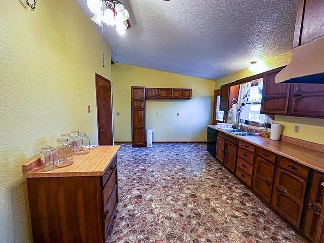 kitchen featuring wooden counters, baseboards, vaulted ceiling, a textured ceiling, and a sink