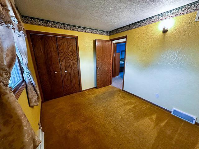 unfurnished bedroom with visible vents, a textured ceiling, a closet, carpet, and a textured wall