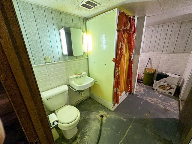 full bath with visible vents, toilet, a sink, wooden walls, and concrete flooring