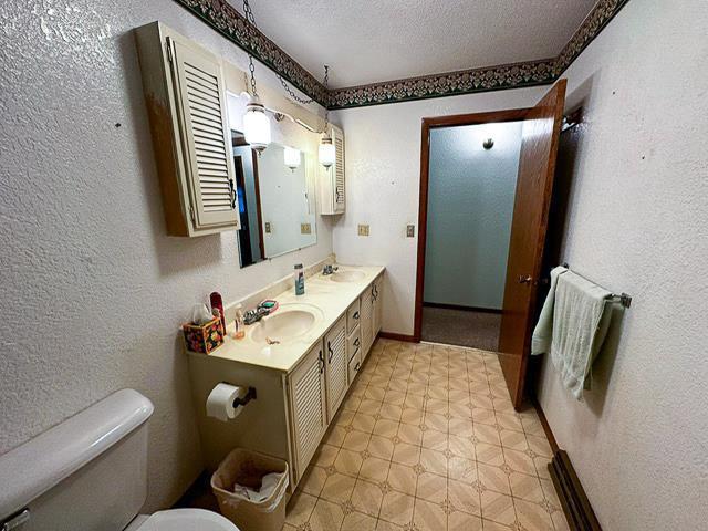 bathroom with a sink, a textured wall, toilet, and a textured ceiling