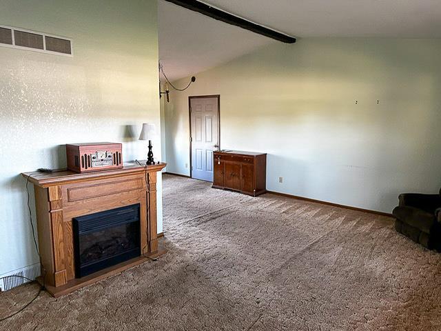 unfurnished living room featuring visible vents, lofted ceiling with beams, a glass covered fireplace, carpet floors, and baseboards