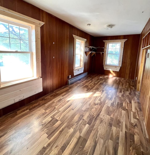 unfurnished bedroom with multiple windows, baseboard heating, and hardwood / wood-style flooring