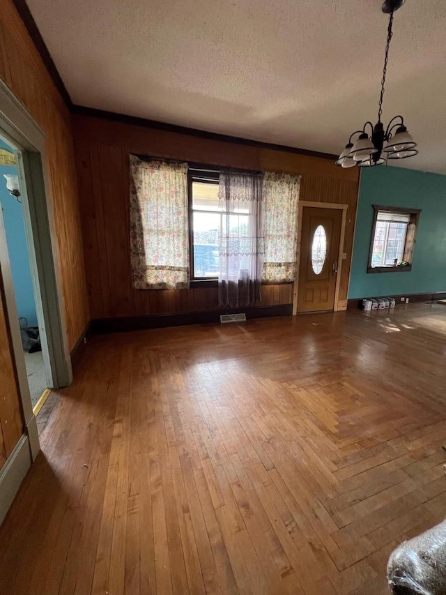 interior space with a notable chandelier, a textured ceiling, wood walls, and hardwood / wood-style floors