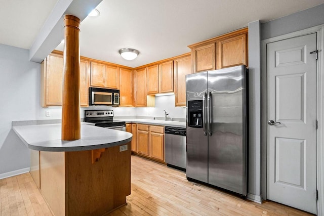 kitchen featuring a kitchen bar, stainless steel appliances, kitchen peninsula, and light hardwood / wood-style floors